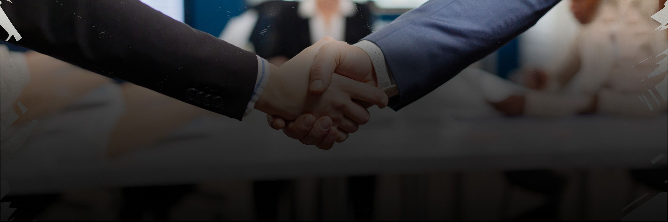 Two individuals shaking hands over a table, symbolizing collaboration and partnership at All In Adventures.